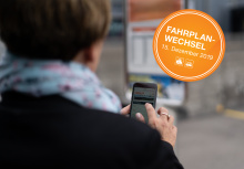 Frau mit Handy in Hand, rechts im Bild ein organger Punkt mit Text: Fahrplanwechsel